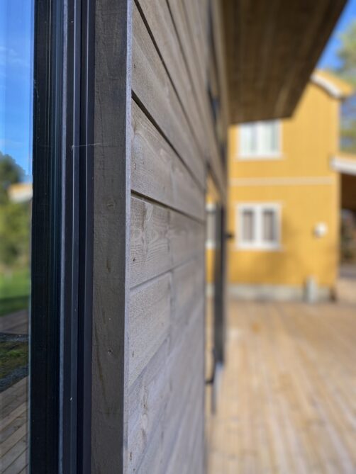 Kledning i front av hytta med gammel hytte i bakgrunn